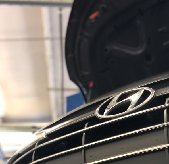 Close-up of Hyundai logo on vehicle grille with hood open in service center